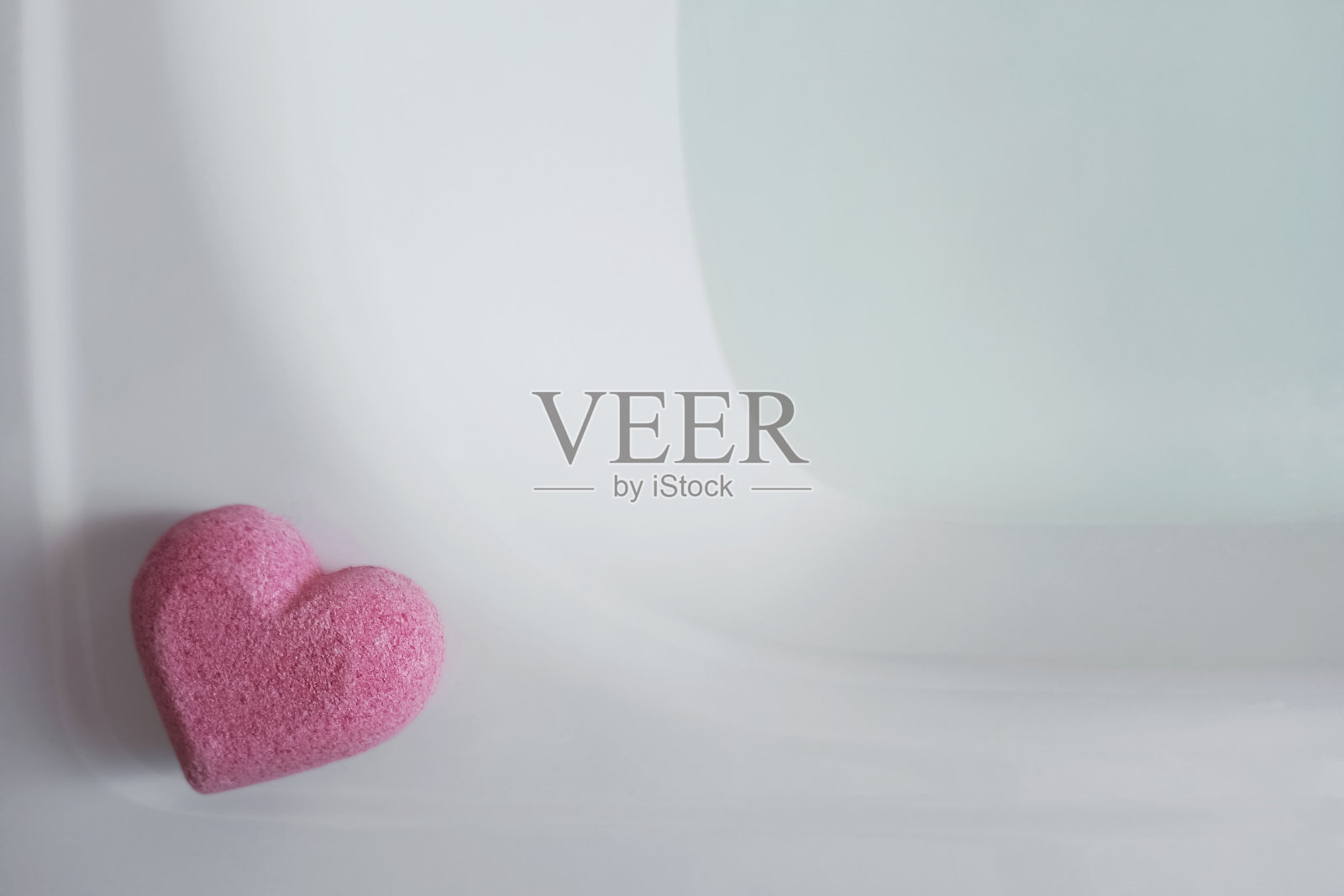 一个粉红色的心形沐浴炸弹放在装满水的浴缸边上。照片摄影图片