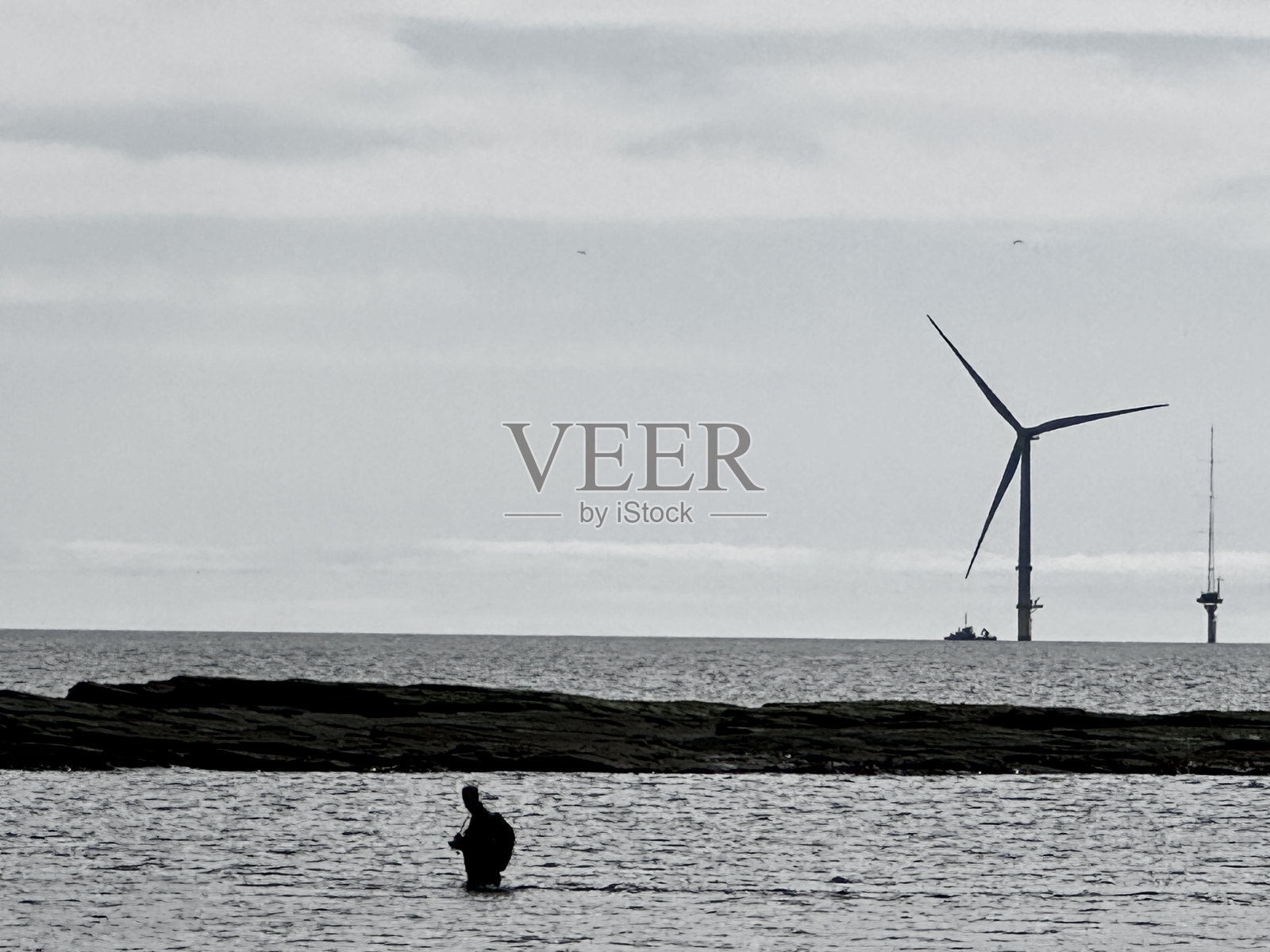 在诺森伯兰郡,一个渔夫走在海上的剪影,背景中有风力涡轮机和船照片摄影图片