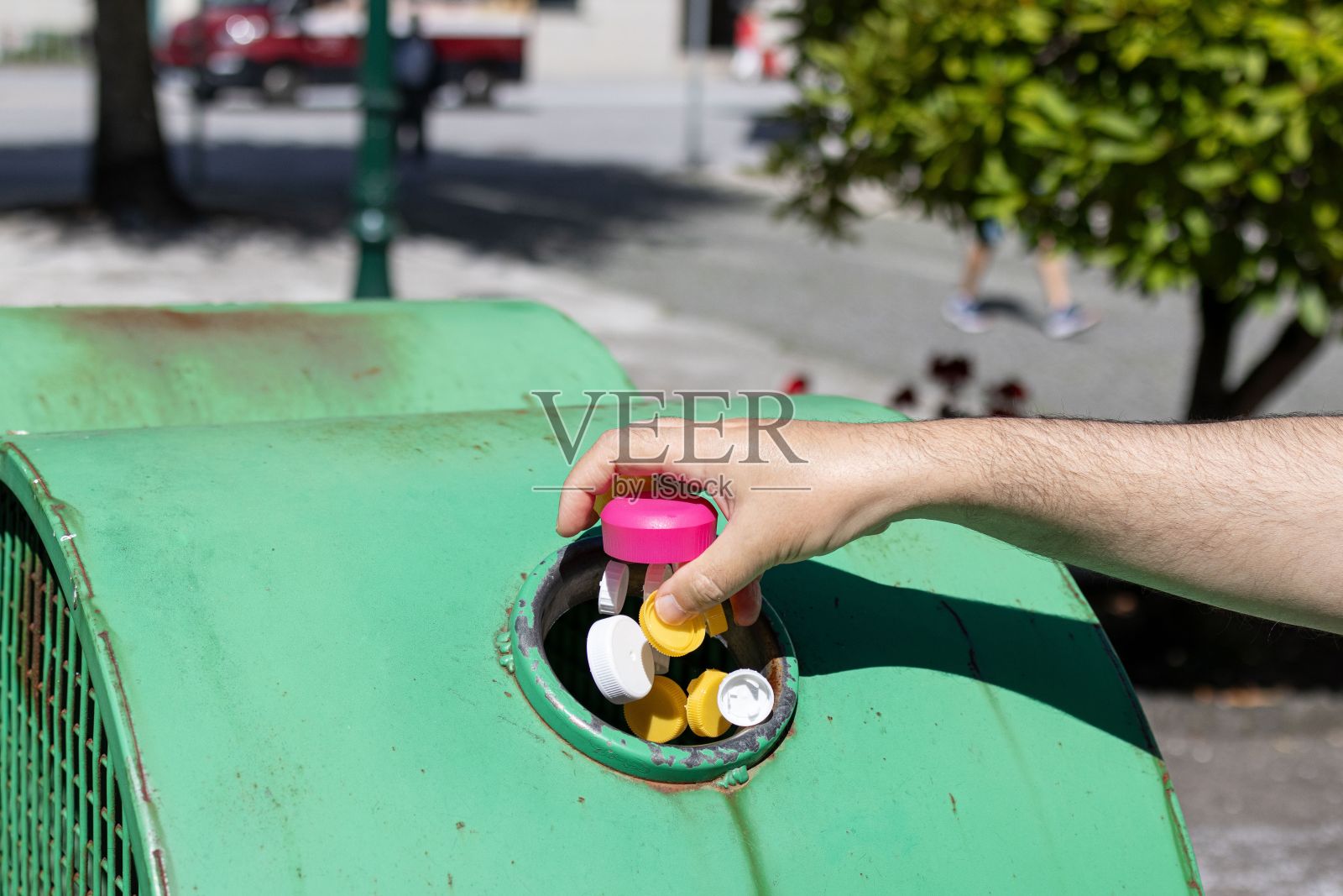 一个人在室外的绿色回收箱里回收塑料瓶盖照片摄影图片