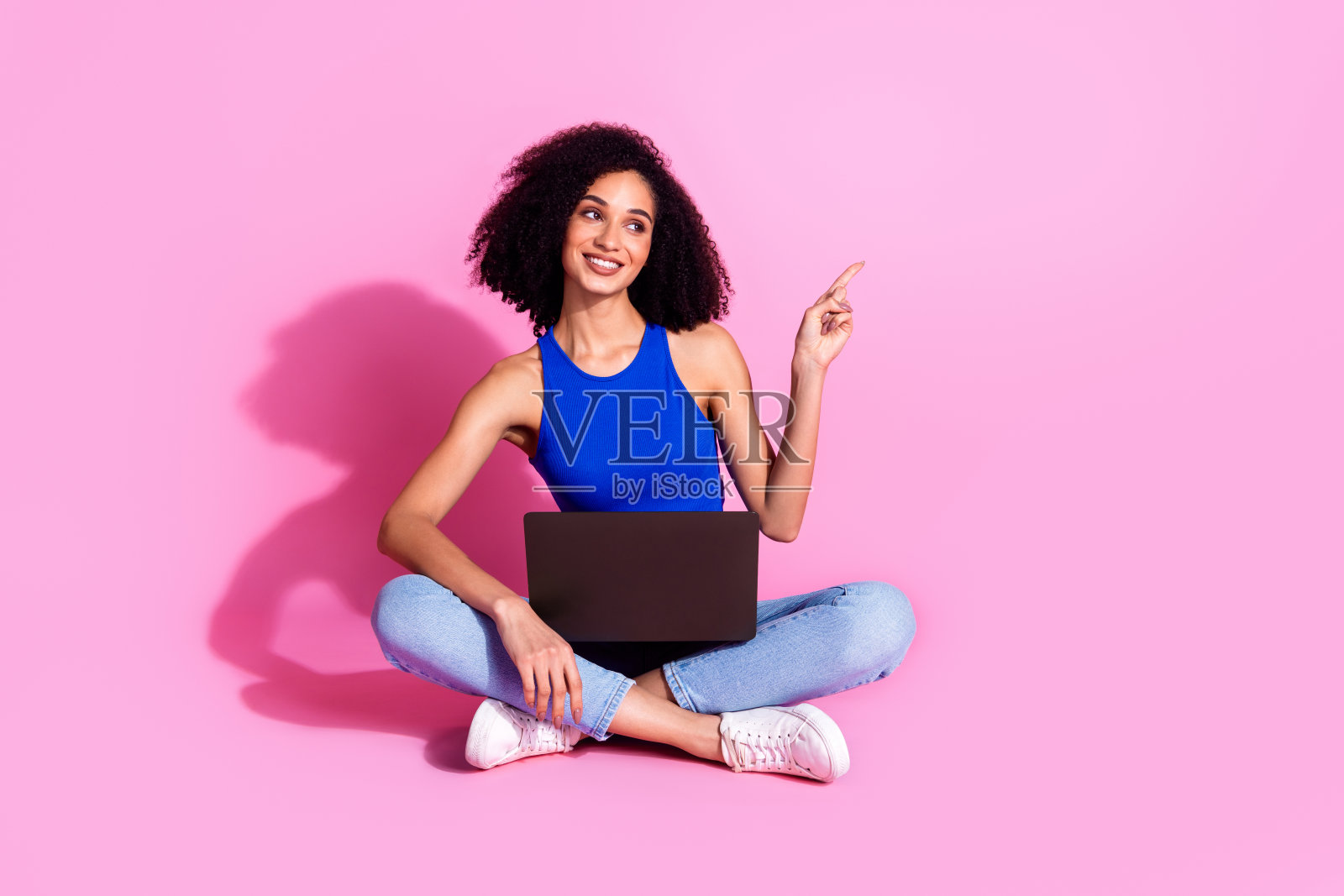 照片中的女孩坐在地板上看空空间指向使用上网本设备孤立的粉红色背景照片摄影图片