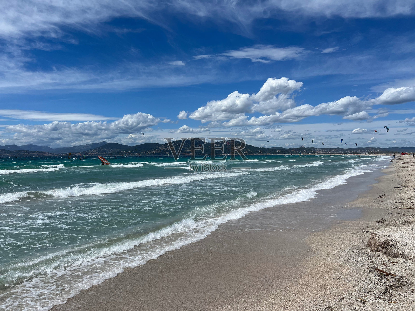 在充满活力的蓝天白云下,海浪和风筝冲浪者的海滩景色照片摄影图片