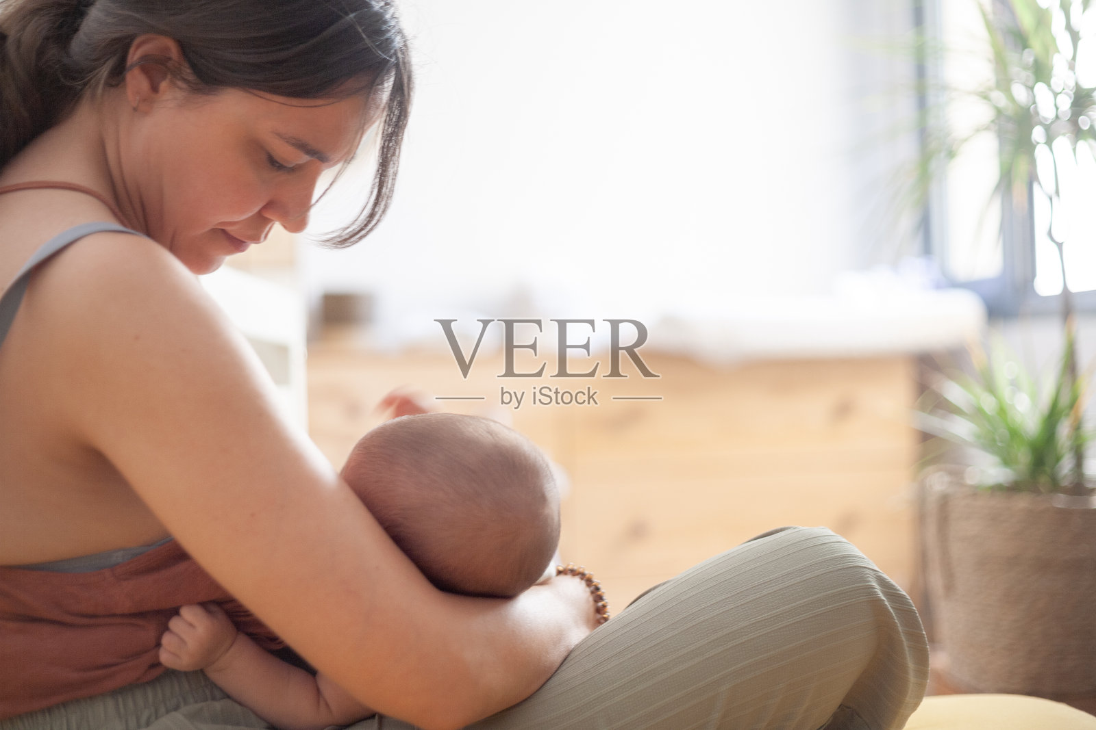 母亲坐在家里卧室的床上给刚出生的女儿喂奶。照片摄影图片