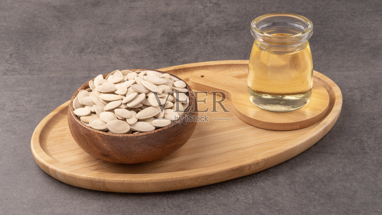装有南瓜籽的木制托盘和玻璃瓶。含有粉末和南瓜籽和油。照片摄影图片