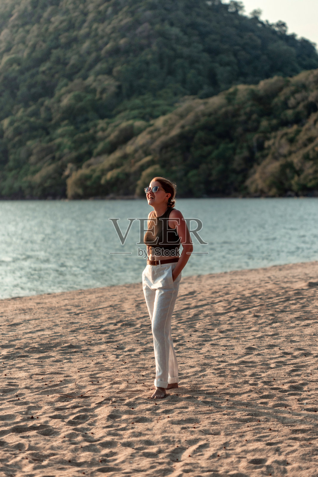 一个年轻美丽的亚洲女人穿着背心和白色裤子在日落的海滩上。沙子。sea.sunset。老财阀风格。用老式镜头拍摄照片摄影图片