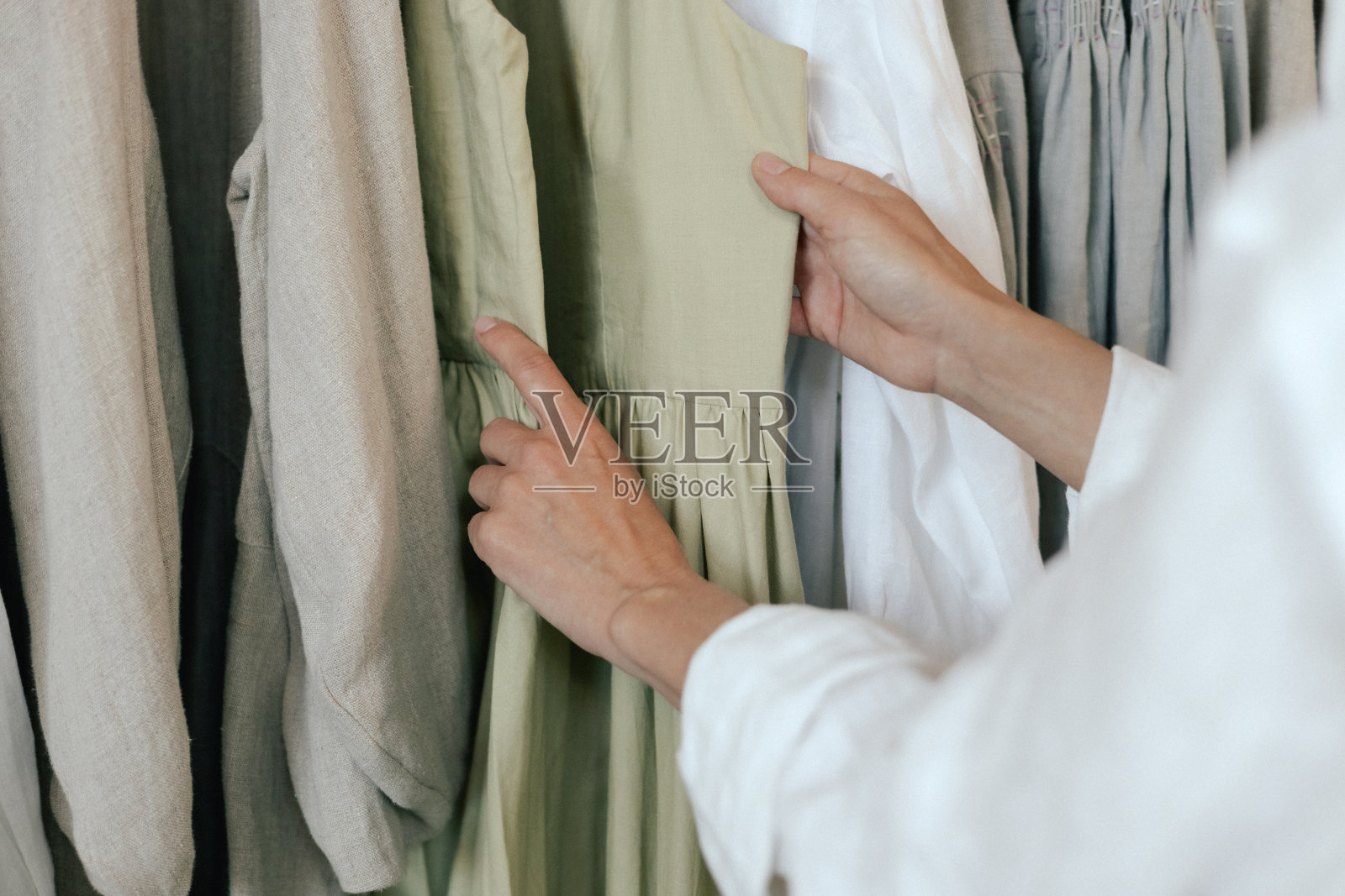 在服装店挑选衣服的女性手拔衣架的特写。一名中年妇女在商场里跑过一排衣服。促销和购物理念。本系列的一部分照片摄影图片