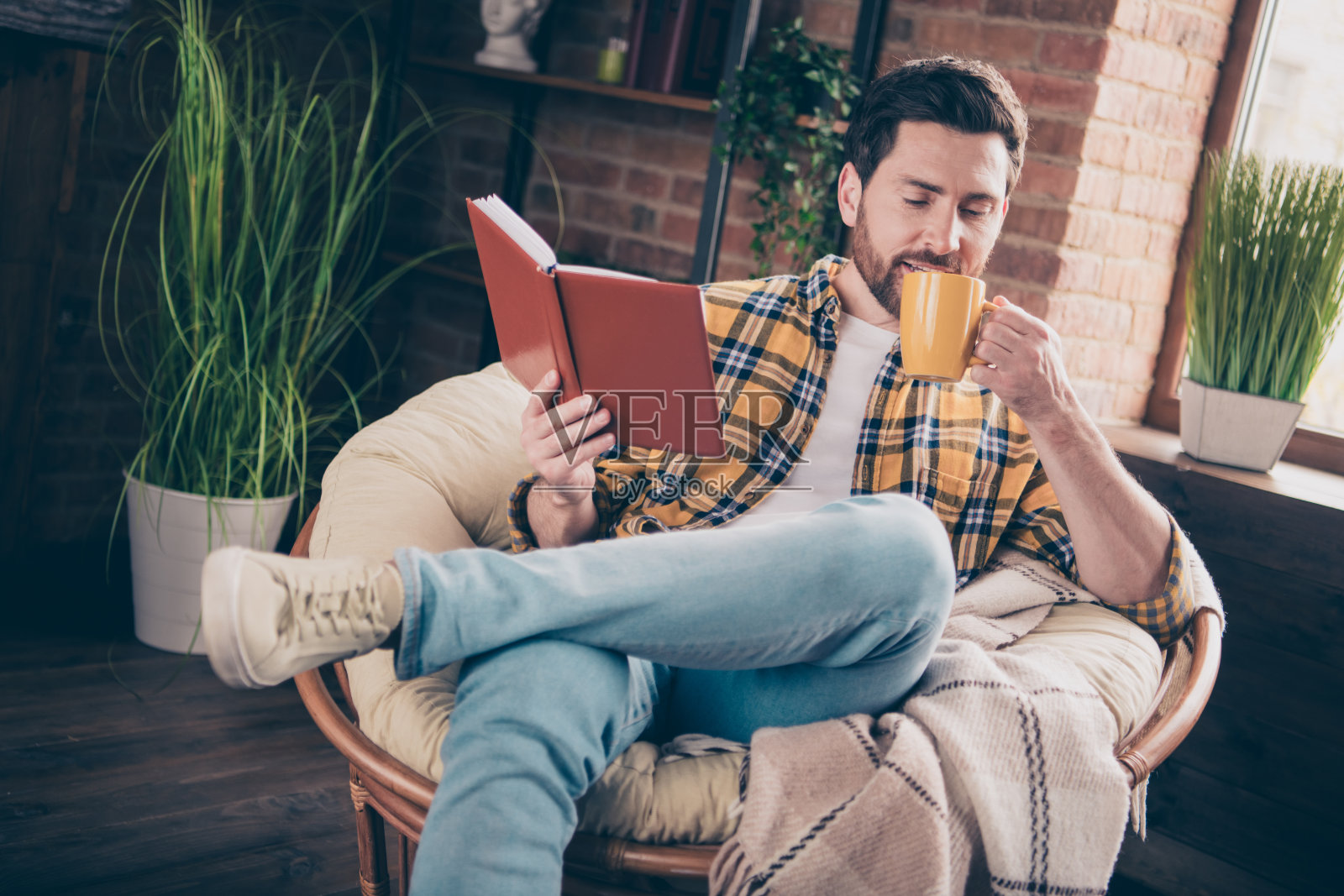 有吸引力的有趣的家伙穿着格子衬衫微笑享受周末阅读小说在房间里享受咖啡在家里的房子照片摄影图片