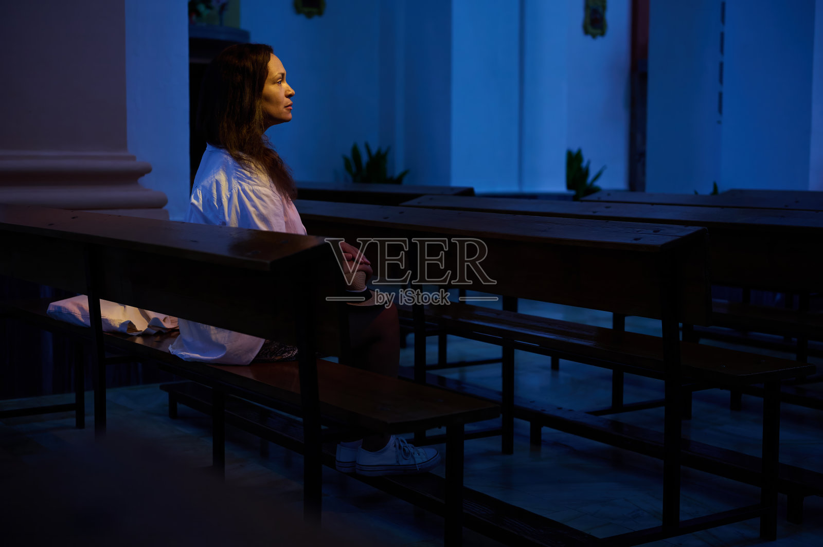 在昏暗的教堂里,一个沉思的女人坐在木凳上照片摄影图片