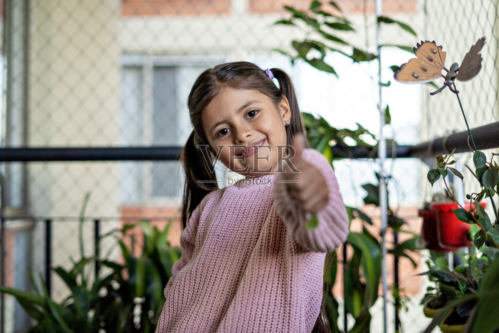 在她公寓的院子里,一个女孩看着相机竖起大拇指的照片。照片摄影图片