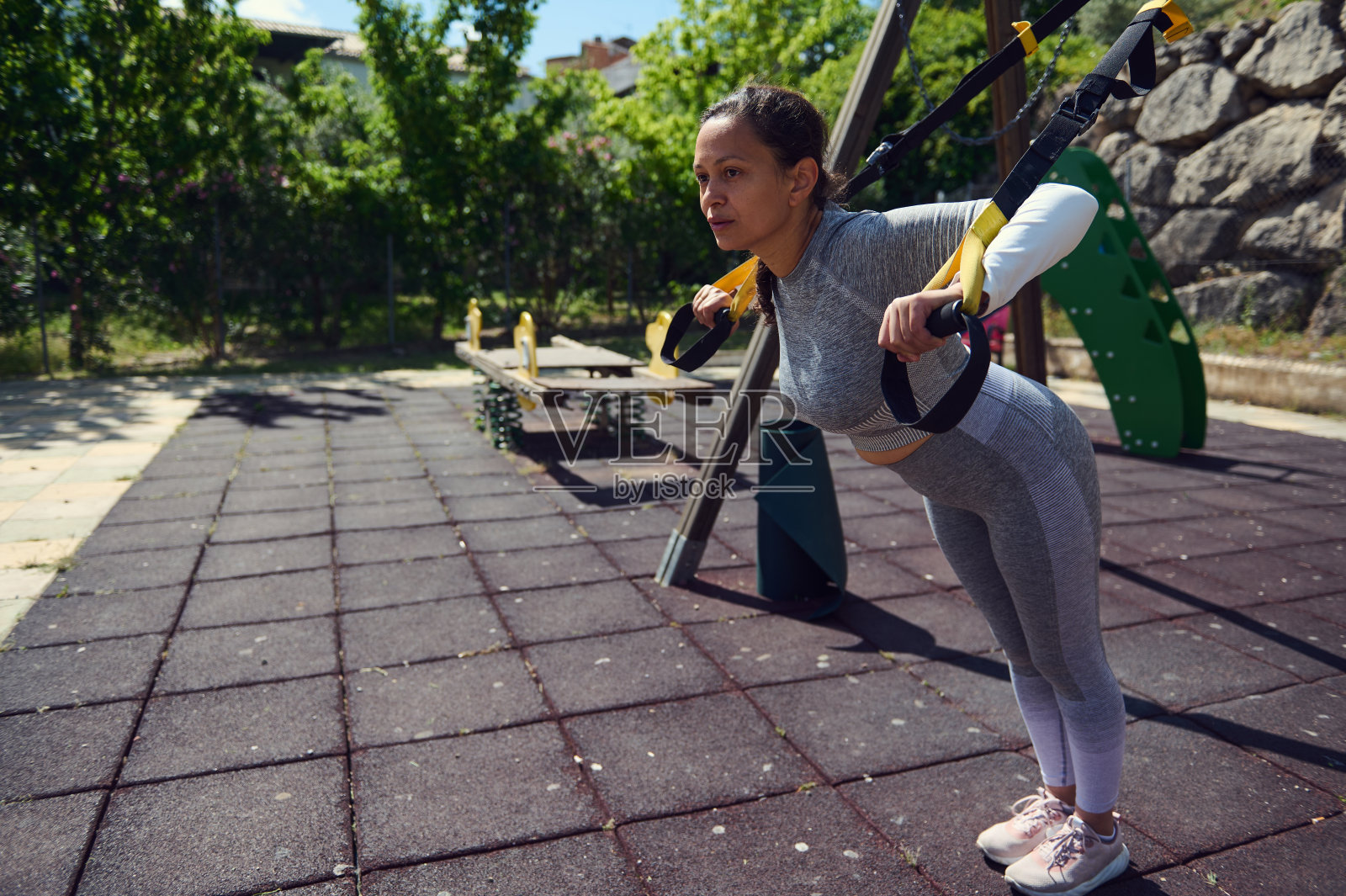 阳光明媚的日子里,年轻女子在户外公园使用悬挂训练器锻炼,展示力量和决心照片摄影图片