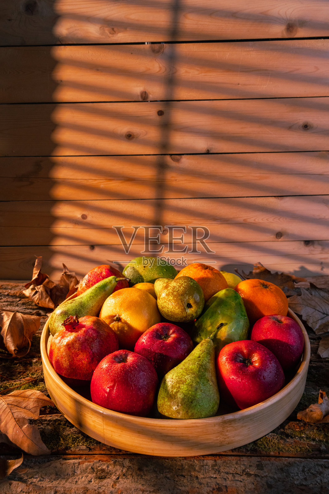 近距离拍摄的新鲜水果在木筐与水滴,秋叶和阳光在篮子和背景-股票照片照片摄影图片