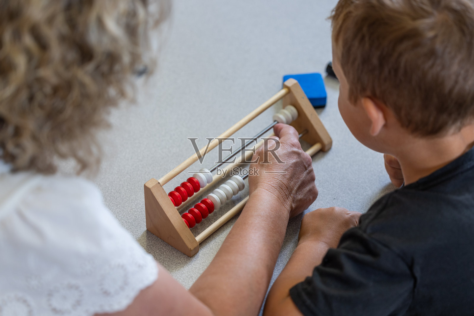 一位老师正在帮助一个小男孩用木算盘照片摄影图片