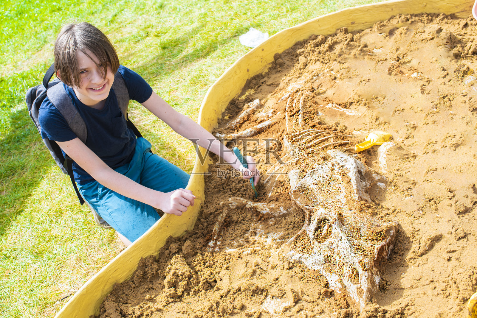 男孩从沙子下挖掘玩具骨头,恐龙骨架。在公园多本体挖掘大师班的孩子。照片摄影图片