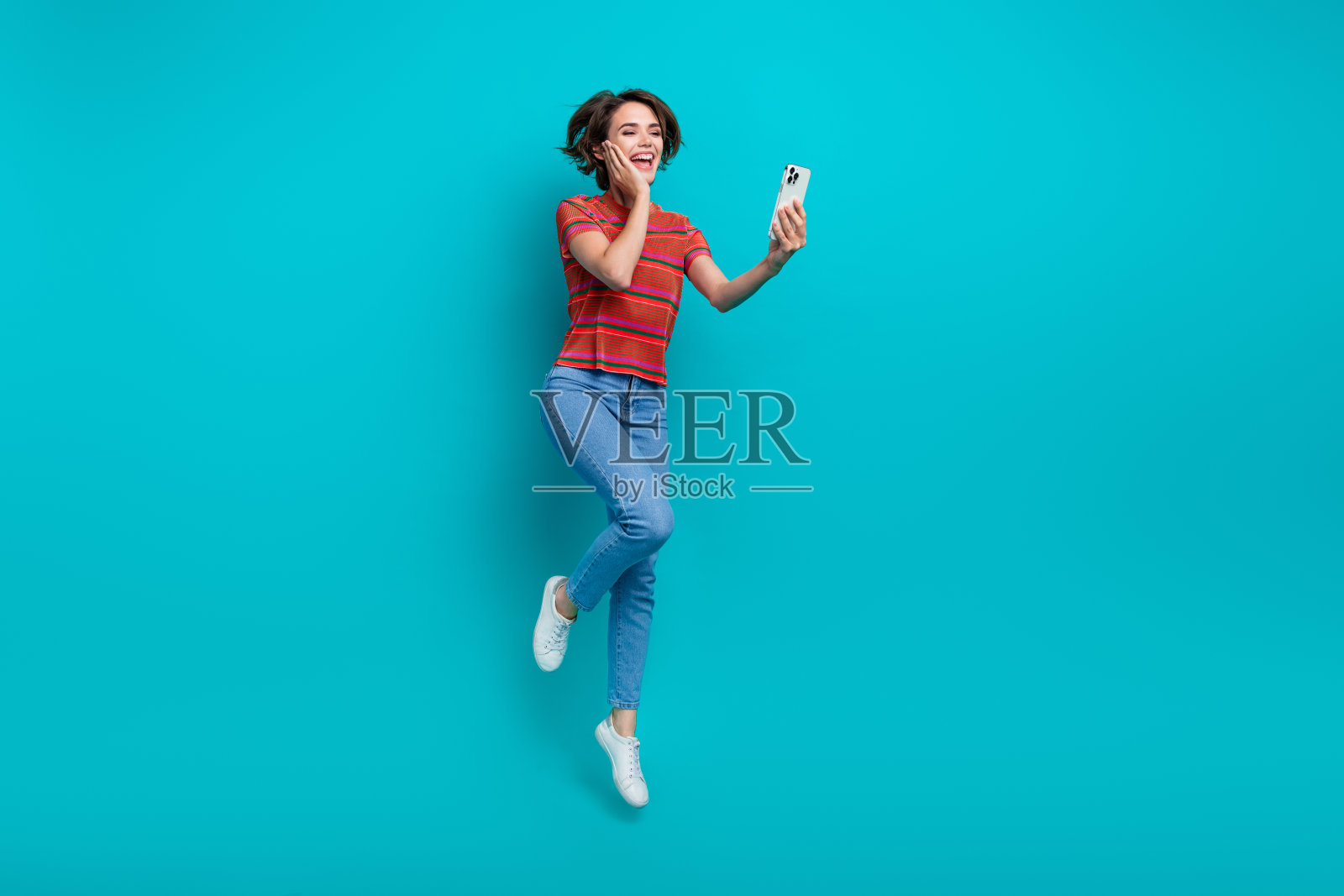 照片中可爱开朗的女孩穿着时髦的衣服在网上聊天,facebook上的电话被隔离在青色背景下照片摄影图片