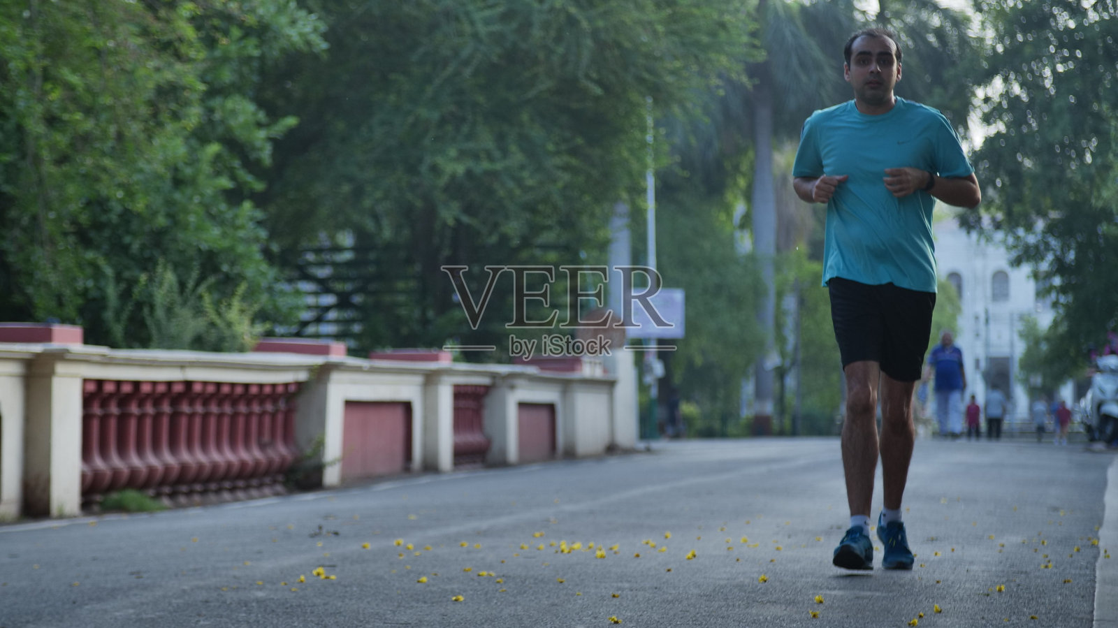一个男人在一条安静的街道上慢跑,背景是树木和红色的篱笆照片摄影图片