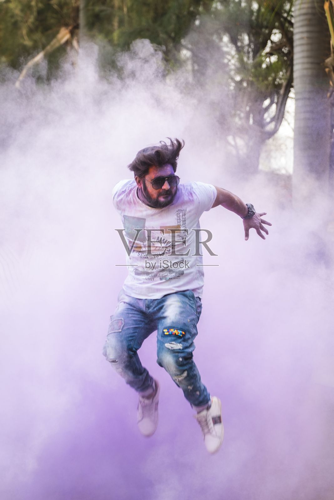 在户外的节日庆祝活动中,一名男子被彩色烟雾包围着在空中跳跃照片摄影图片