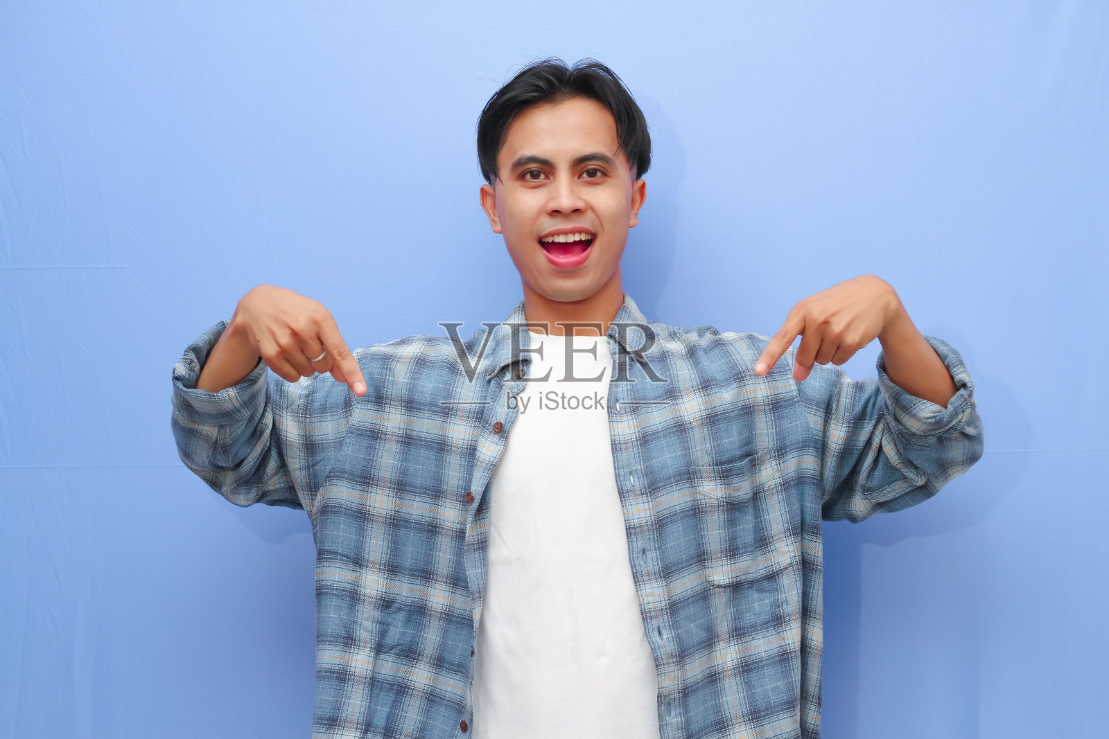 兴奋快乐的年轻亚洲人摆姿势,用手指指着蓝色背景上的空白拷贝空间。照片摄影图片