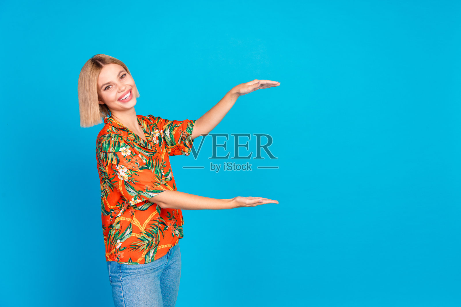 照片中开朗可爱的女孩穿着时髦的橙色印花衣服,在蓝色的背景上保持空白照片摄影图片
