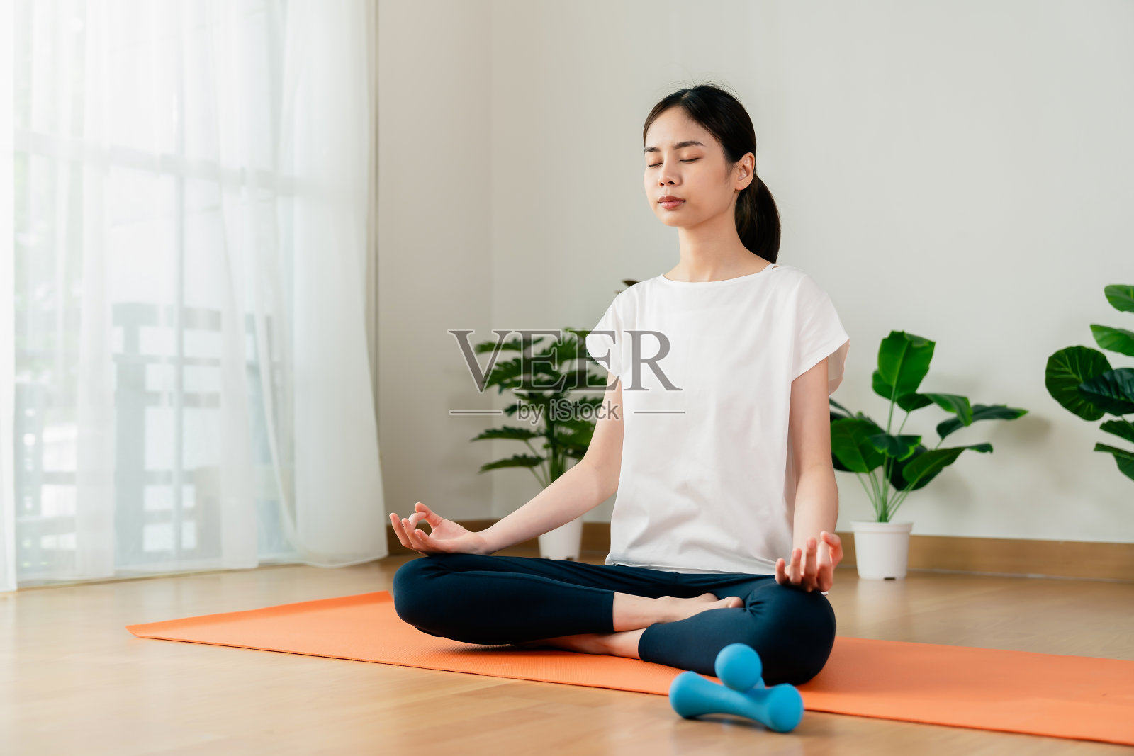 一个女人坐在地板上做莲花式,在家里练习瑜伽时冥想。照片摄影图片