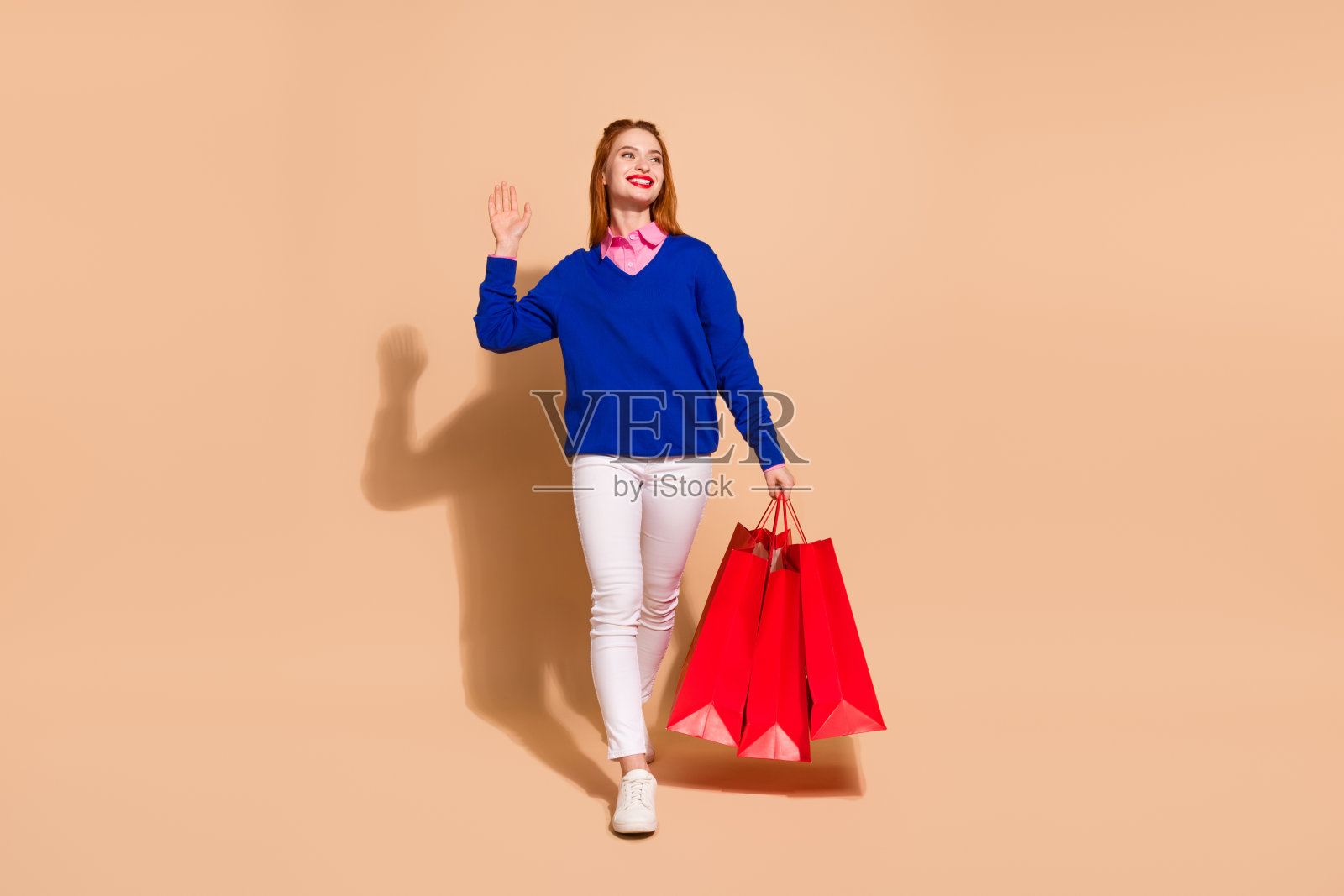 漂亮的年轻女子走商店的全尺寸照片,手臂挥动空的空间,穿着米色背景上孤立的套头衫照片摄影图片