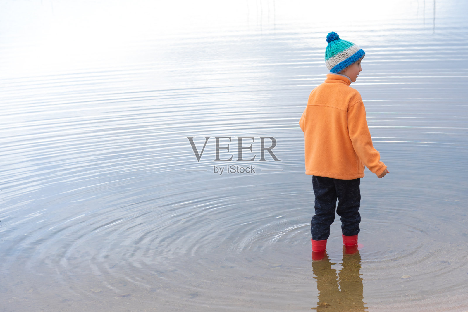 一个男孩在寒冷的日子里穿着长筒雨靴穿过一个湖照片摄影图片