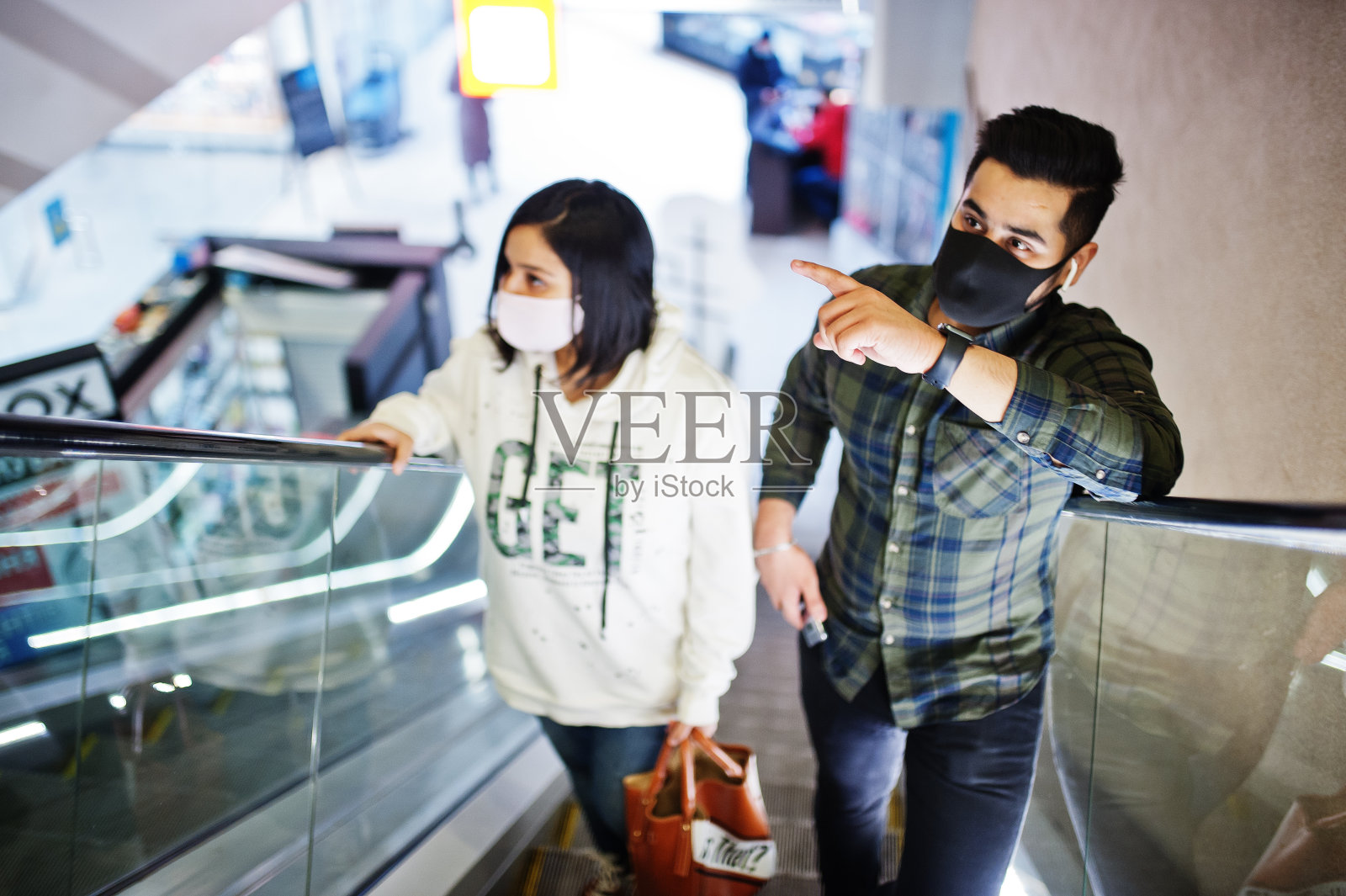 一对戴着口罩的亚洲夫妇爬上贸易中心的自动扶梯。照片摄影图片