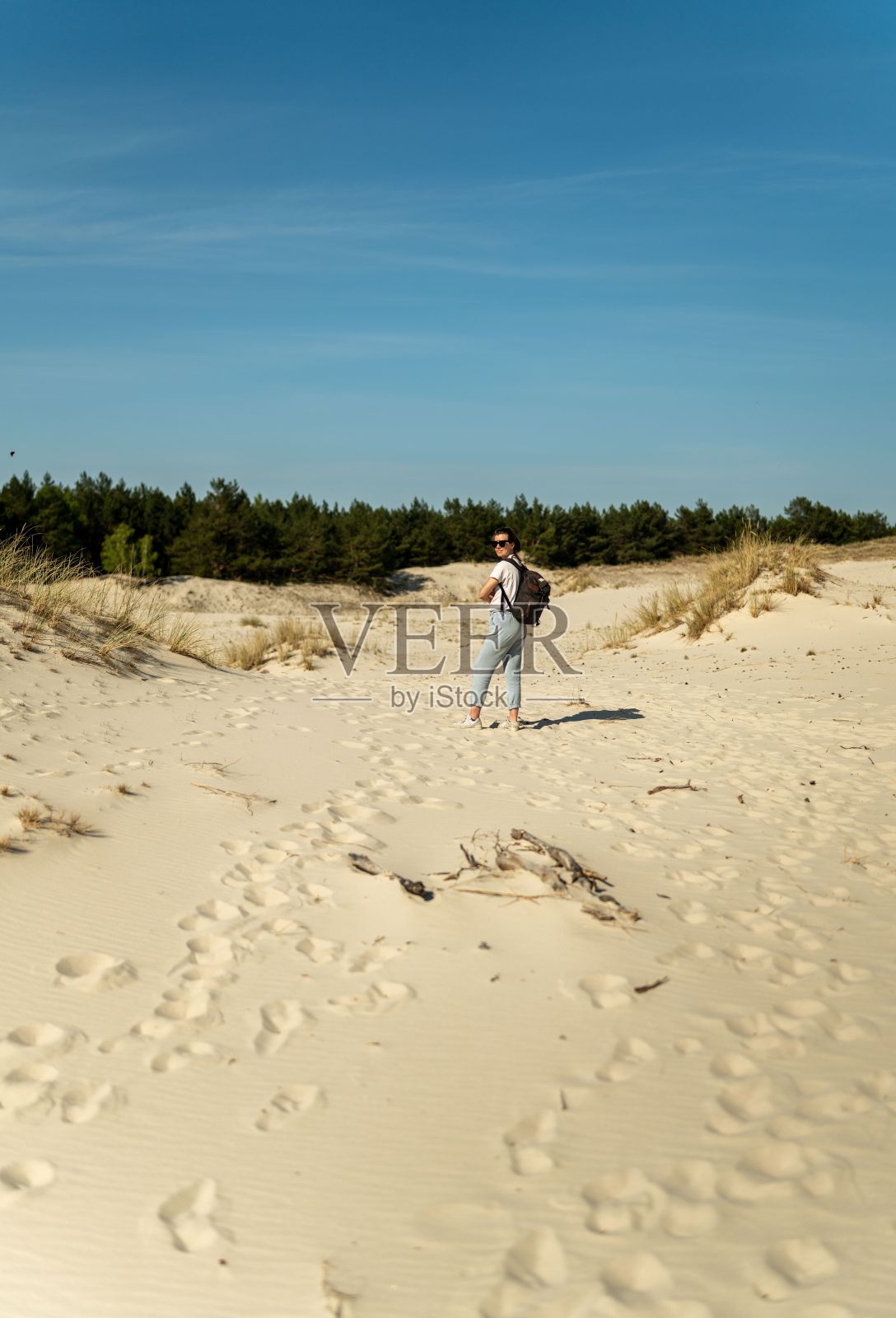 在波兰晴朗的蓝天下,一名妇女背着背包徒步穿越沙丘照片摄影图片