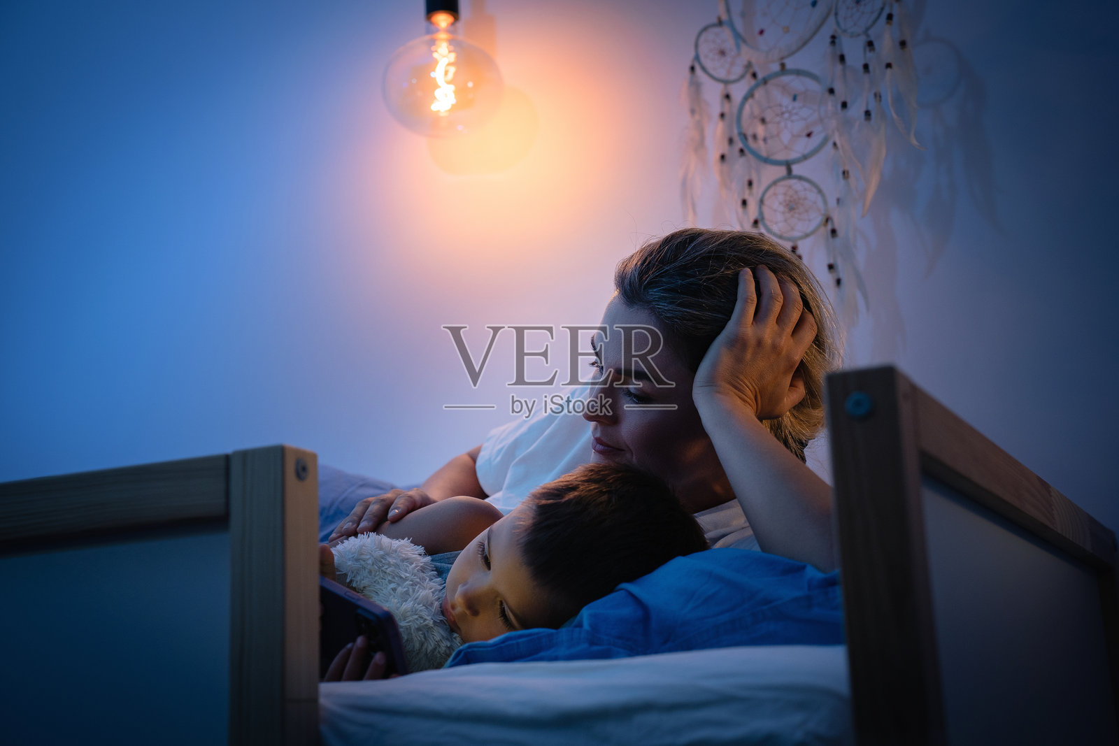 母亲和儿子晚上在床上一起看智能手机照片摄影图片
