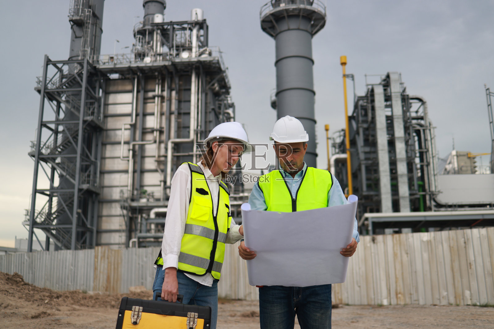 一对维护工程师,带着工具箱和蓝图,在一个新安装的热电厂项目中进行检查。照片摄影图片