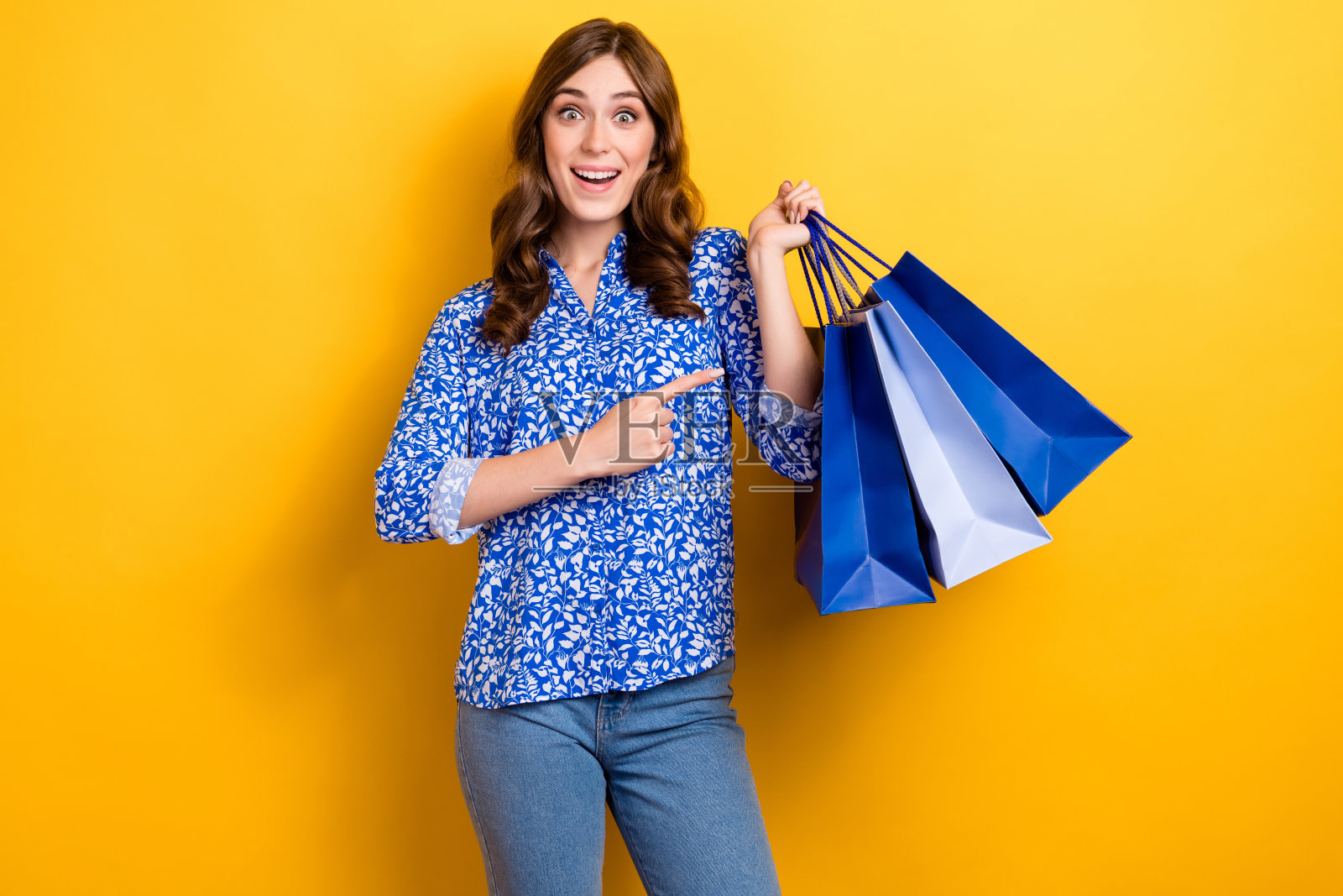 照片中,开朗漂亮的女士穿着时髦的衣服,拿着黄色背景的低价衣服照片摄影图片