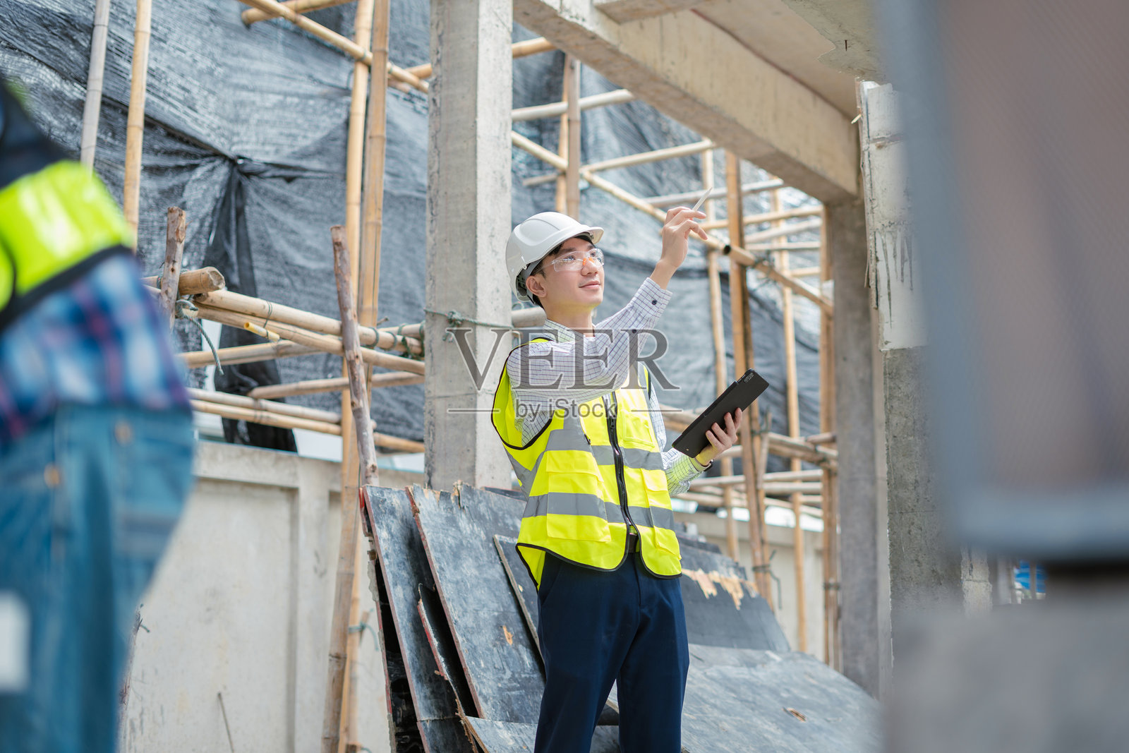 男建筑工程师或建筑师戴安全帽,在施工现场使用卷尺。照片摄影图片