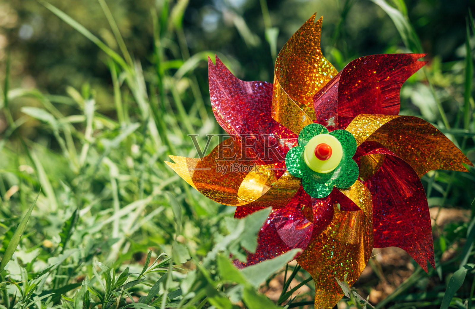 塑料彩色的风车旋转着,被风吹在花园光滑的绿叶表面上。玩具风车。童年的概念。照片摄影图片