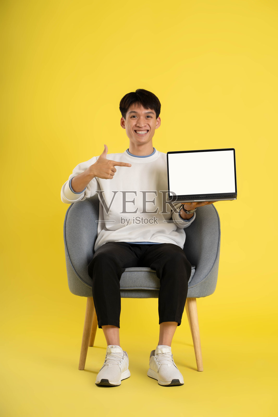 穿着毛衣的亚洲年轻人的全身,用黄色背景的笔记本电脑照片摄影图片