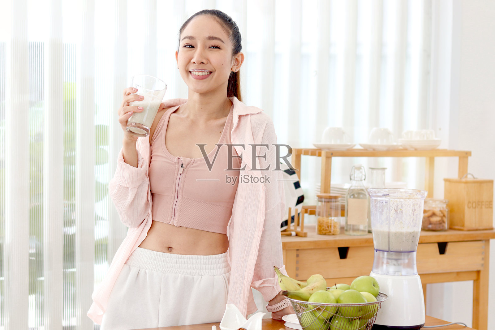 健身运动服的运动女孩在厨房里喝着混合水果和蔬菜制成的健康奶昔饮料。美丽快乐微笑的亚洲女人试图减肥,苗条和健康。照片摄影图片