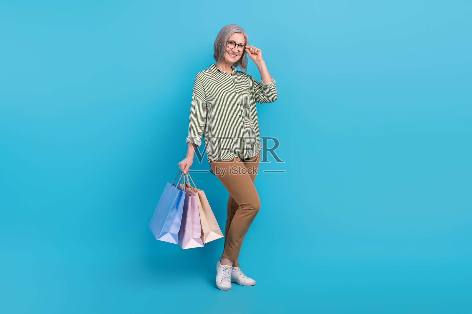 全身照片甜美迷人的女士穿着条纹衬衫,戴着眼镜,手持购物者孤立的蓝色背景照片摄影图片
