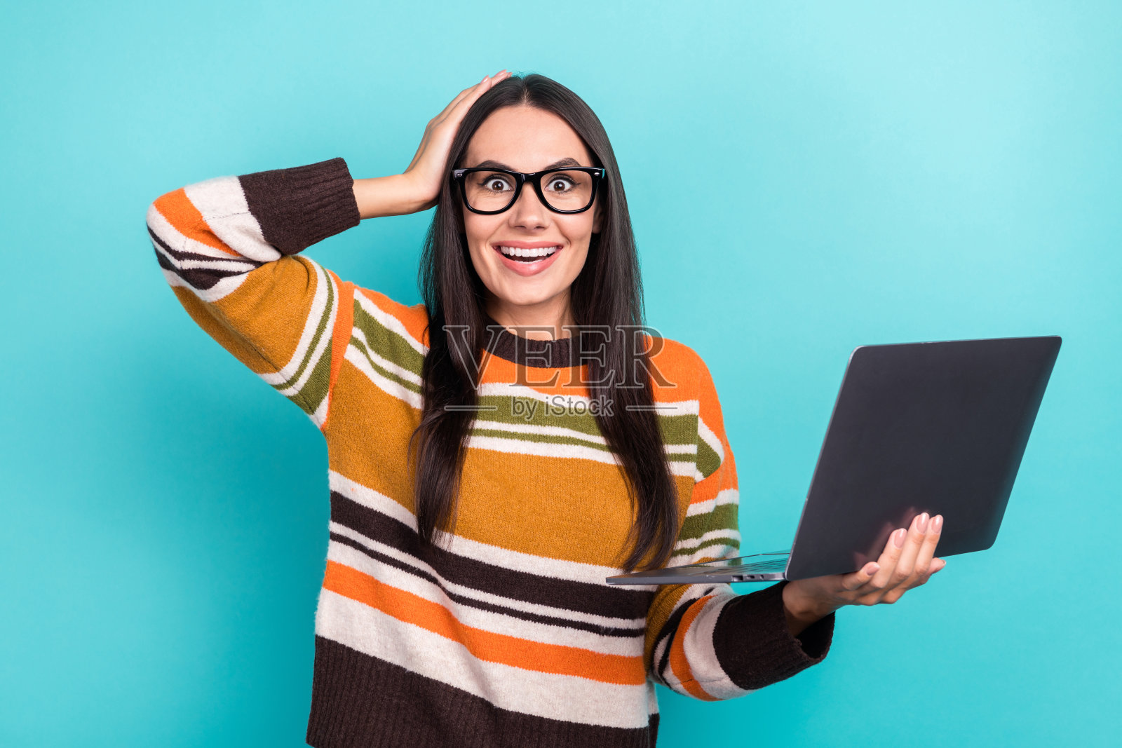 照片迷人的年轻有趣的女人穿着时尚的橙色毛衣,手,头,拿着她的设备震惊流行的视频孤立的青色背景照片摄影图片