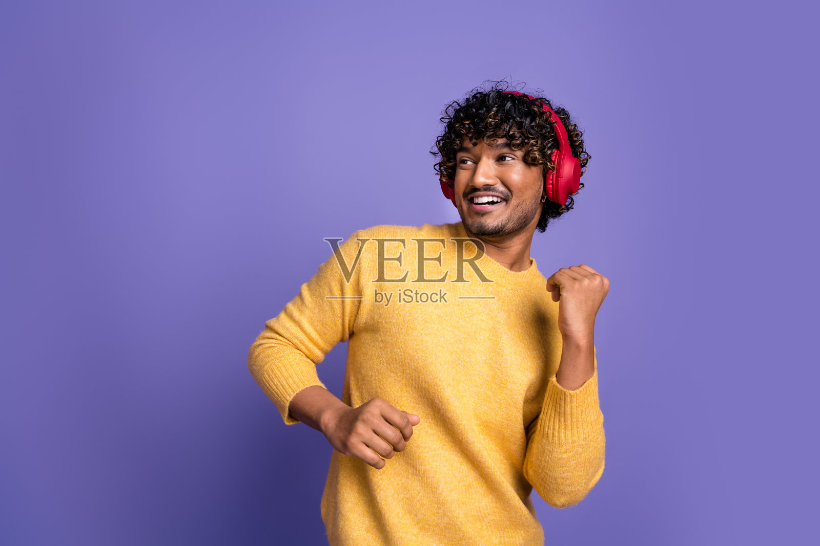 时髦积极的男人的照片,穿着时髦的黄色衣服,听音乐,现代科技孤立在紫色的背景照片摄影图片