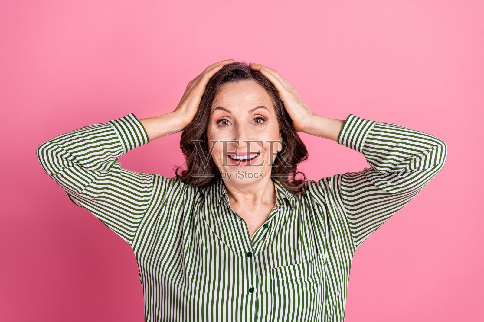 漂亮的老年妇女的肖像手臂触摸头穿条纹衬衫孤立的粉红色背景照片摄影图片