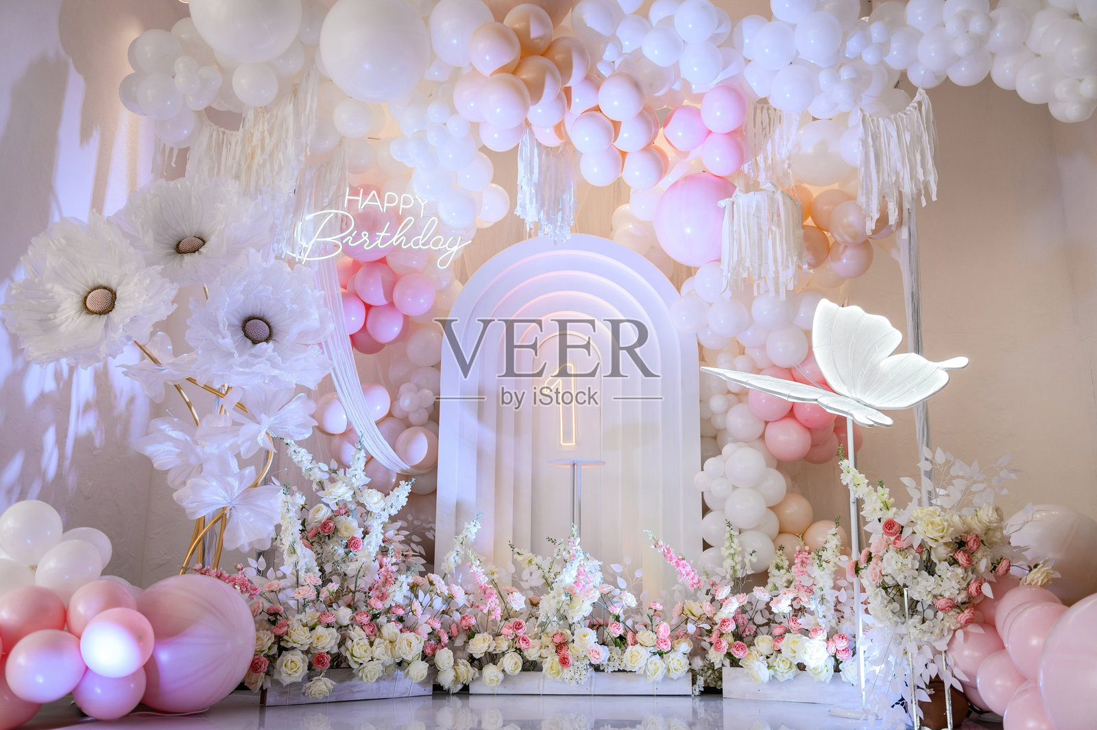 儿童照相区。背景照片墙上1岁女孩的生日派对。粉红色的拱门装饰,白色的气球,生日快乐的文字,鲜花,蝴蝶纸装饰。照片摄影图片