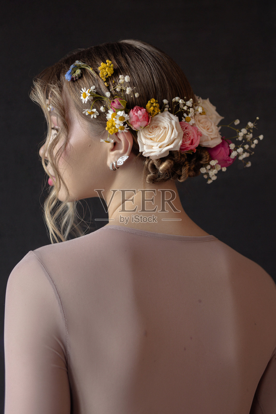 一个有着长长的金色卷发的女人,头戴花假发,身穿一件轻薄的浅棕色长袖上衣。她在看镜头外的什么东西照片摄影图片