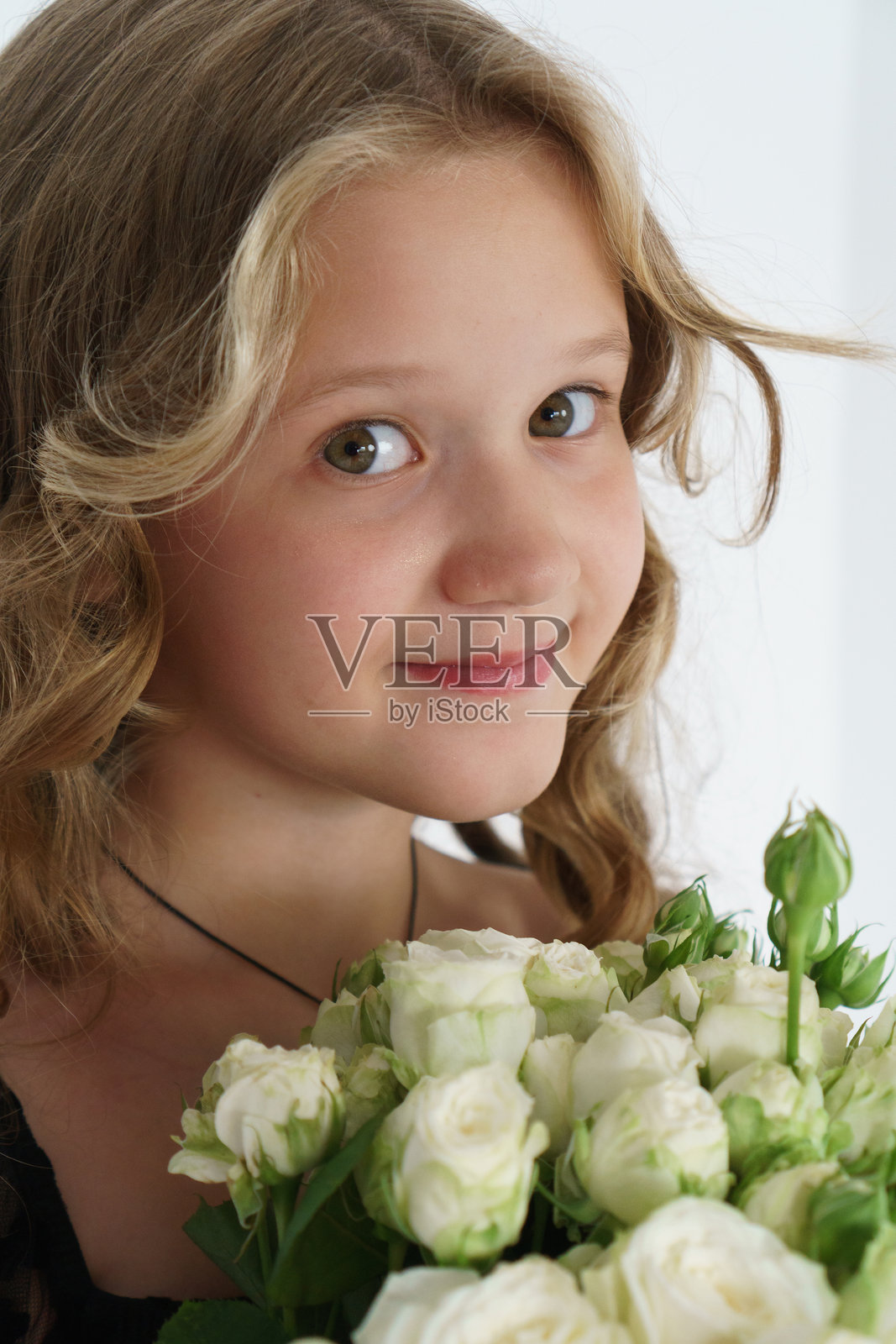 一个有着绿色眼睛和长长的卷发的女孩的肖像,她手里拿着一束白色的灌木玫瑰。照片摄影图片