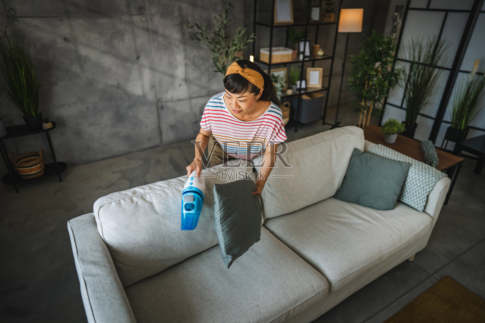 成熟的日本女人在家里用手吸尘机吸尘沙发照片摄影图片