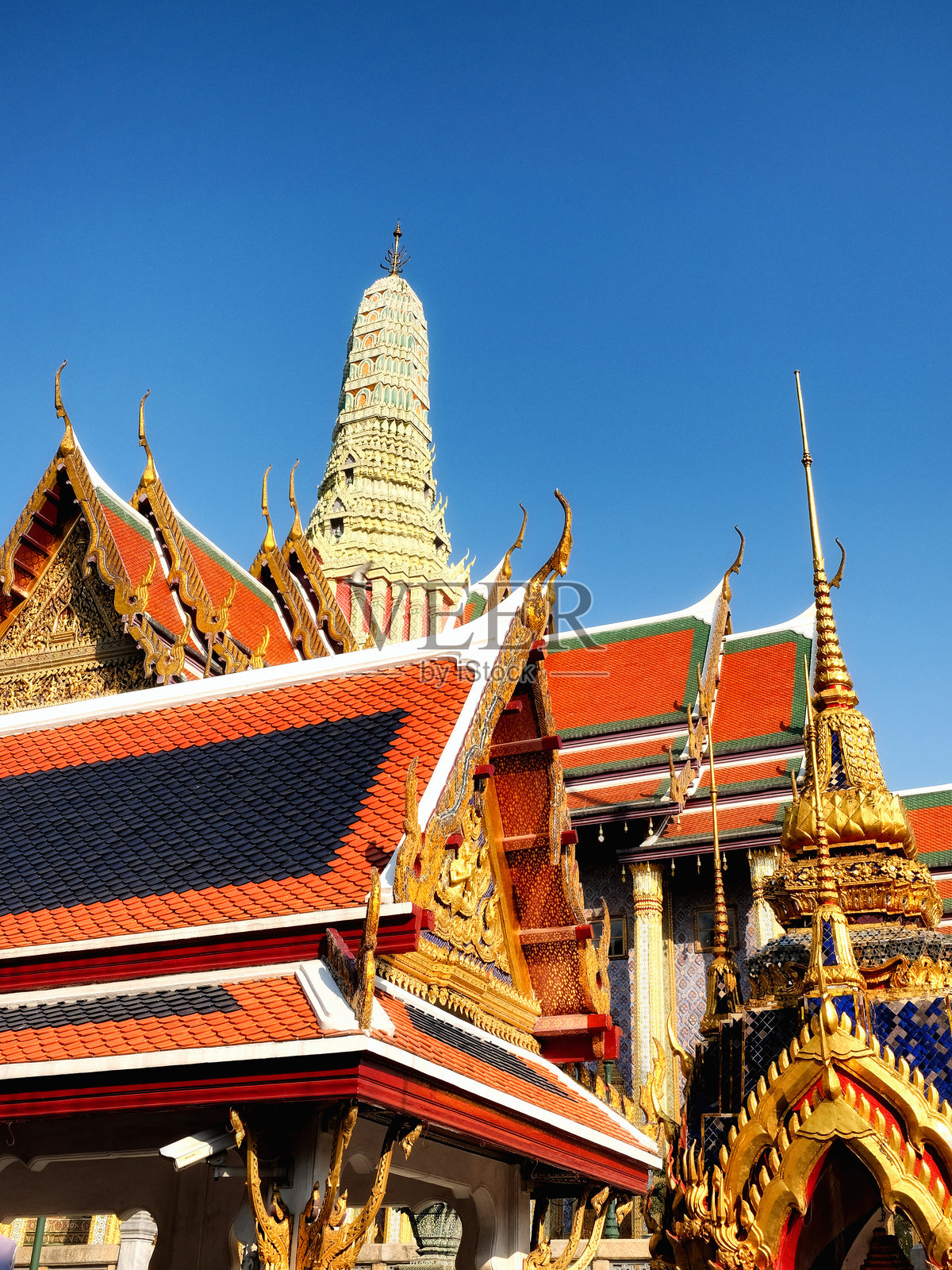 一个迷人的低角度的泰国寺庙显示其深红色的屋顶,镀金的装饰,和一个高耸的白色尖塔设置在一个原始的蔚蓝的天空的背景下。照片摄影图片