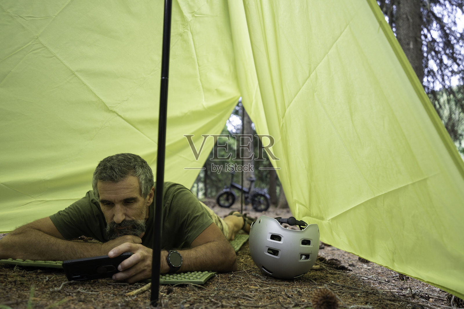 自行车打包和露营。一名男子在森林里的帐篷里用手机放松。照片摄影图片
