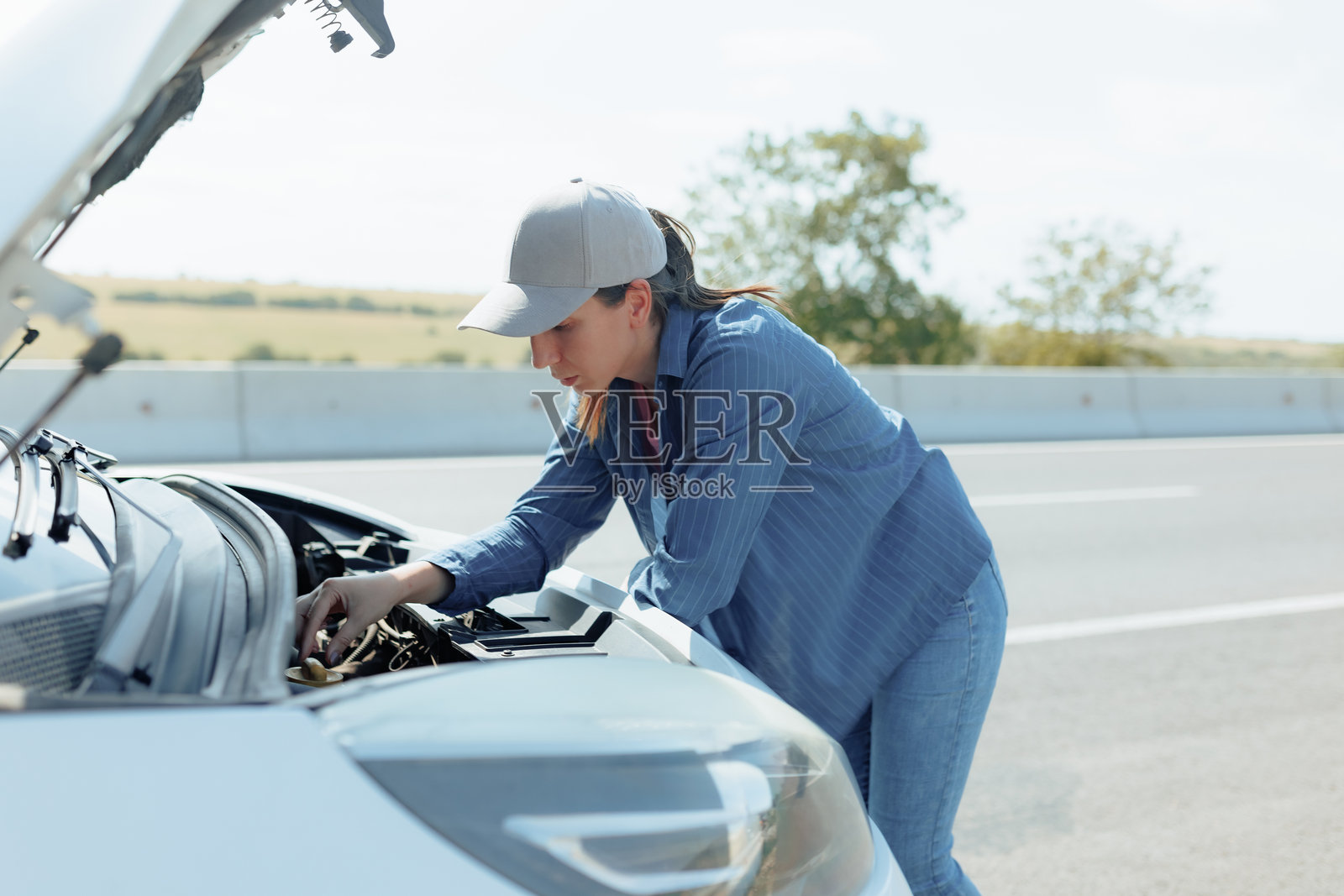 忧心忡忡的黑发女人用她的破车检查引擎故障照片摄影图片