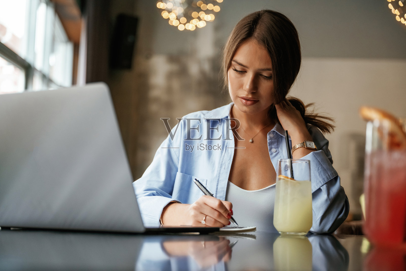 用笔写信息。拿着笔记本电脑的美女在酒吧里照片摄影图片