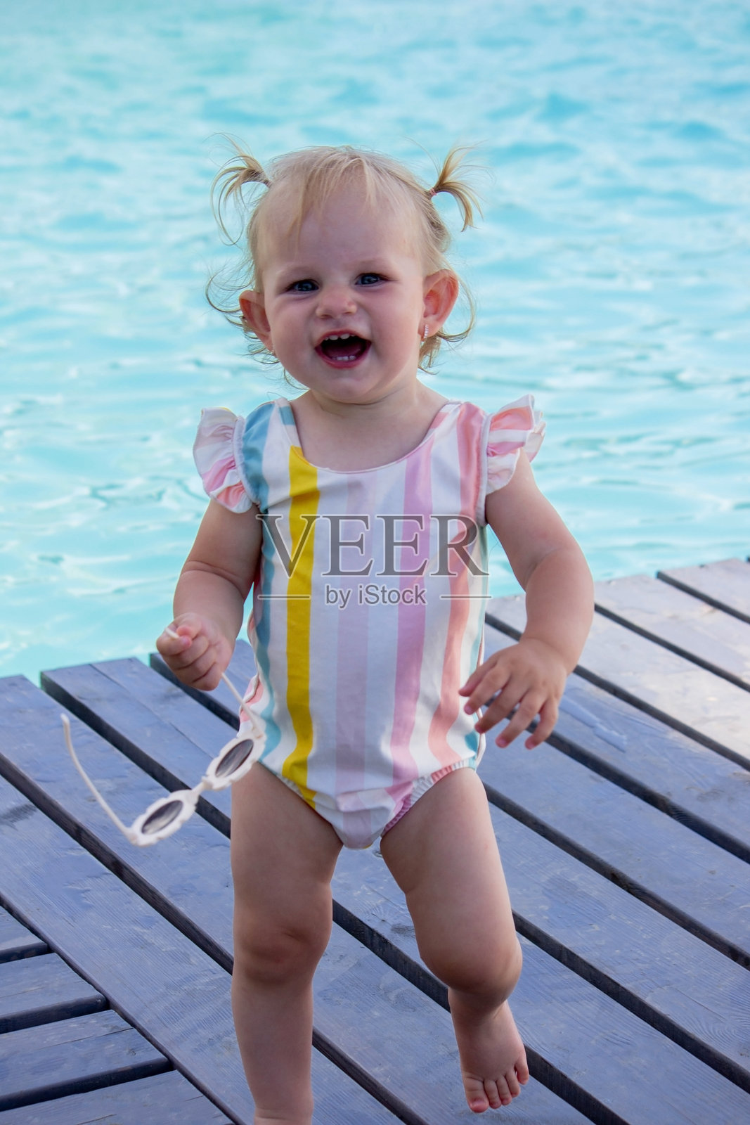 小女孩在泳池的背景上穿着漂亮的泳衣和太阳镜。休息。照片摄影图片