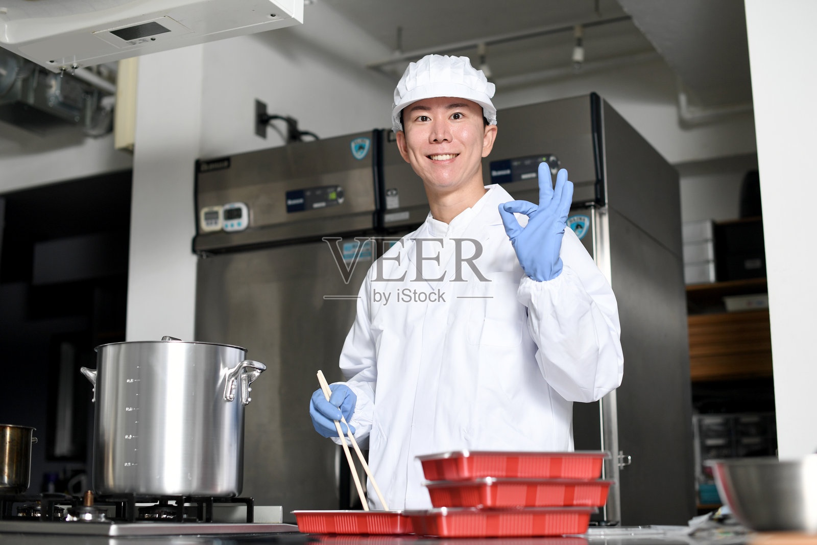 一名穿着干净西装的男厨师一边往便当盒里装食材,一边摆好姿势。照片摄影图片