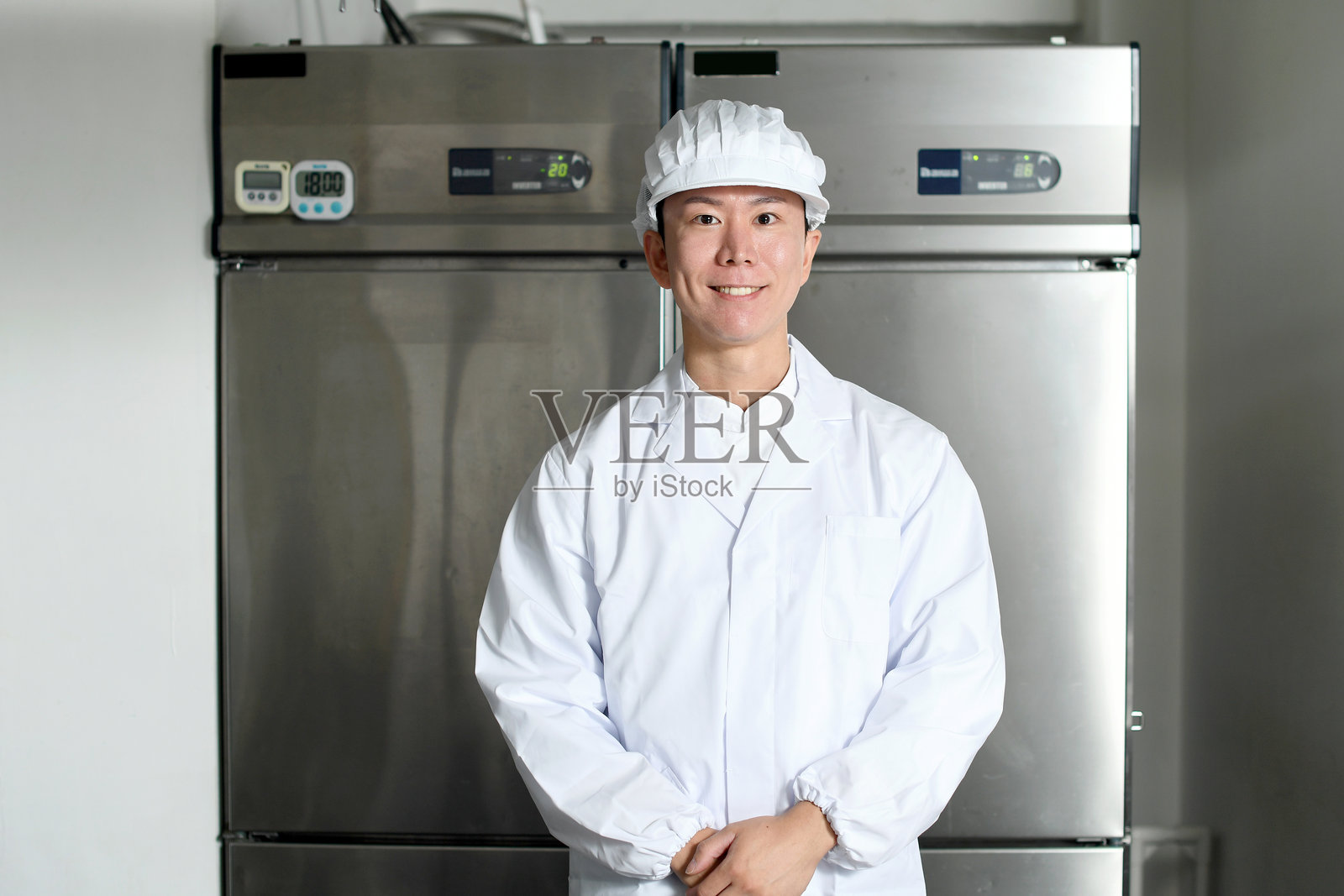 一名穿着卫生服的亚洲男子微笑着站在厨房的大冰箱前照片摄影图片