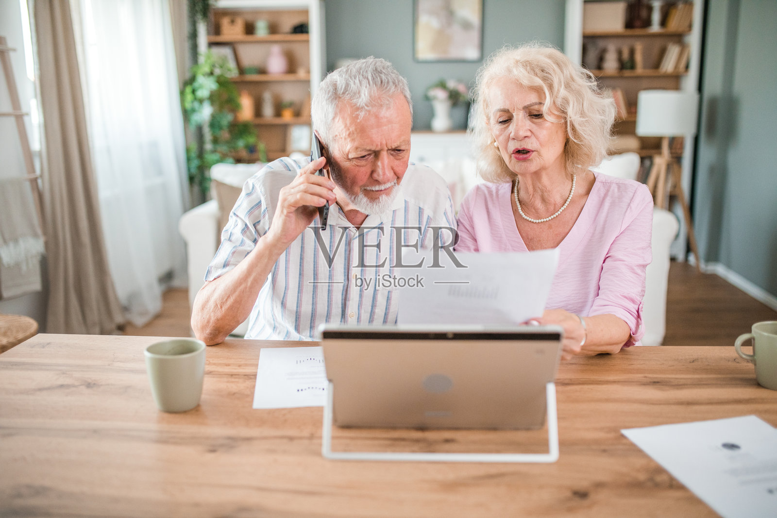 一对忧心忡忡的老年夫妇试图解决他们的经济问题。一位资深人士正在用手机与一位银行顾问讨论此事照片摄影图片