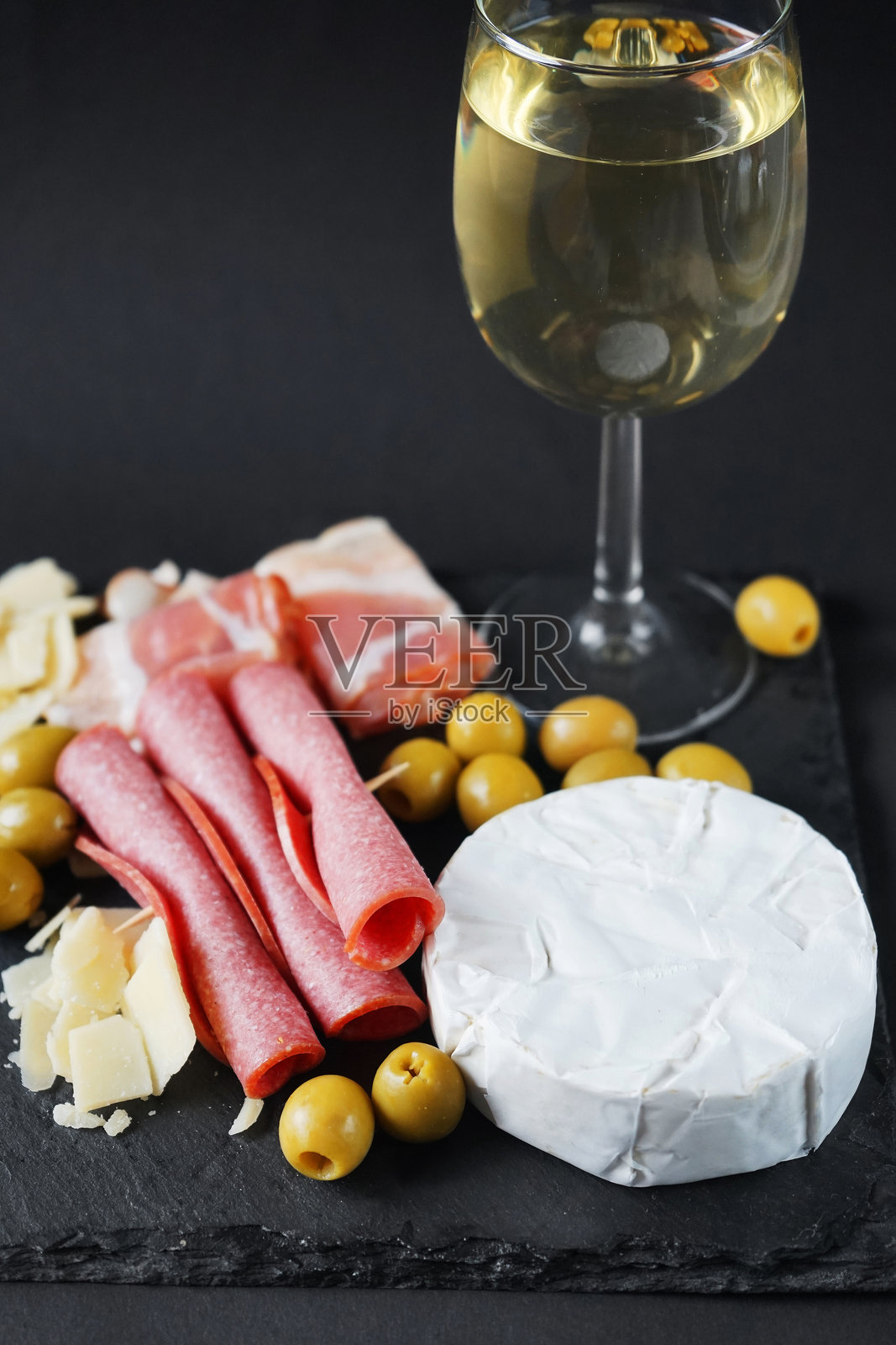 布里干酪配意大利腊肠、培根、帕尔马干酪、橄榄,托盘上放一杯白葡萄酒照片摄影图片